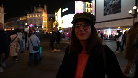 woman smiling in piccadilly circus at night, surrounded by crowds and illuminated city lights. london