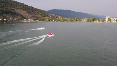 Drohnenaufnahmen-Aus-Der-Luft,-Die-Einem-Roten-Motorboot-Auf-Dem-Bielersee-Folgen-Und-Das-Blaue-Wasser-Und-Die-Wunderschöne-Landschaft-Zeigen