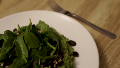risotto de espinacas verdes adornado en un plato de cerámica blanca con un tenedor metálico al lado