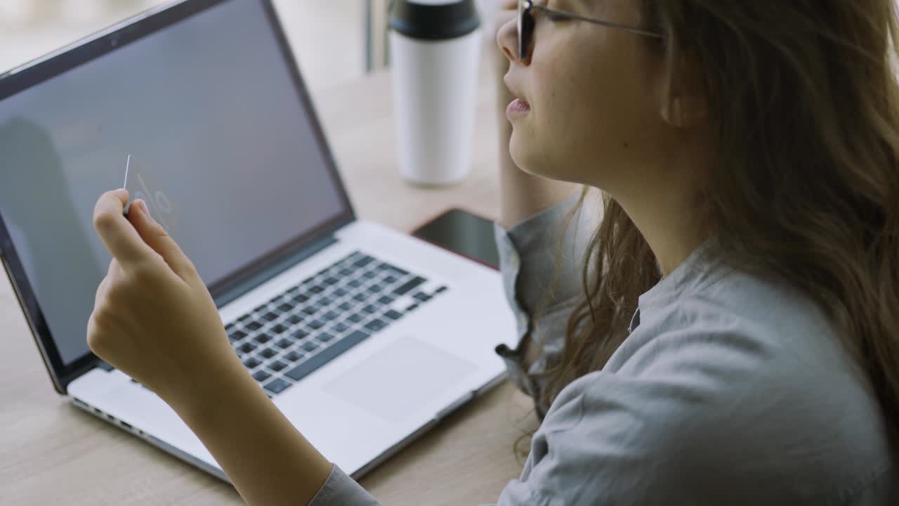 mujer sostiene una tarjeta de crédito usando una computadora portátil en la mesa