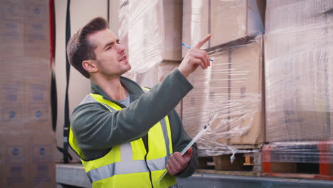 male freight haulage worker with clipboard checking lorry being loaded with boxes