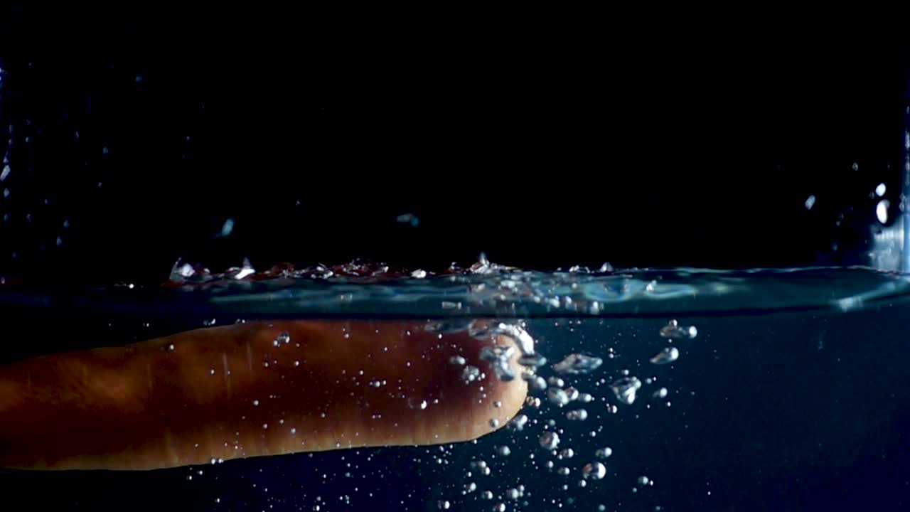 high speed camera slow motion reverse video of an orange carrot splashing into the water. Black background