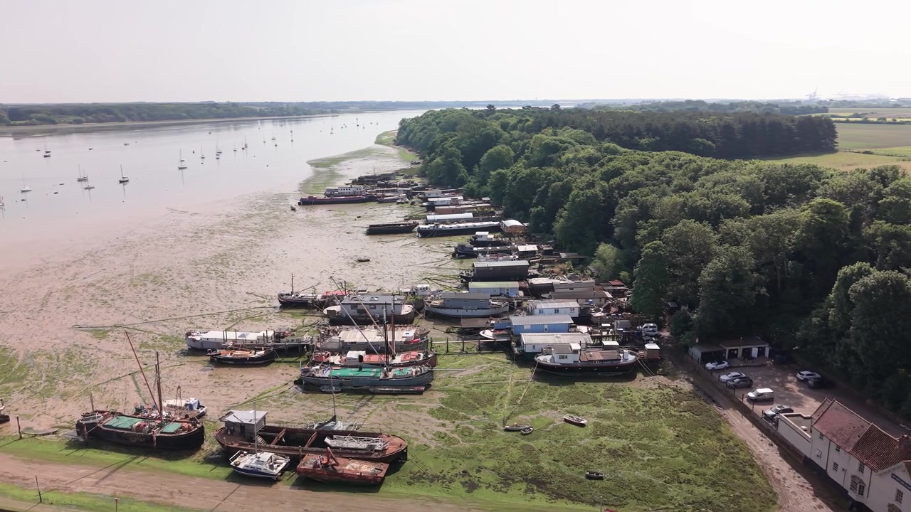 Luftfoto af fortøjede både og bygninger langs floden ved siden af frodigt skovområde ved lavvande