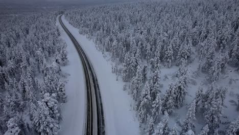 aerial drone view of road surrounded by winter wonderland forest in lapland, finland, arctic circle