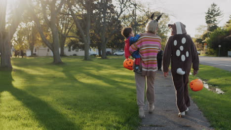 mom with two children in carnival costumes in honor of halloween. walking down the street of a small american town