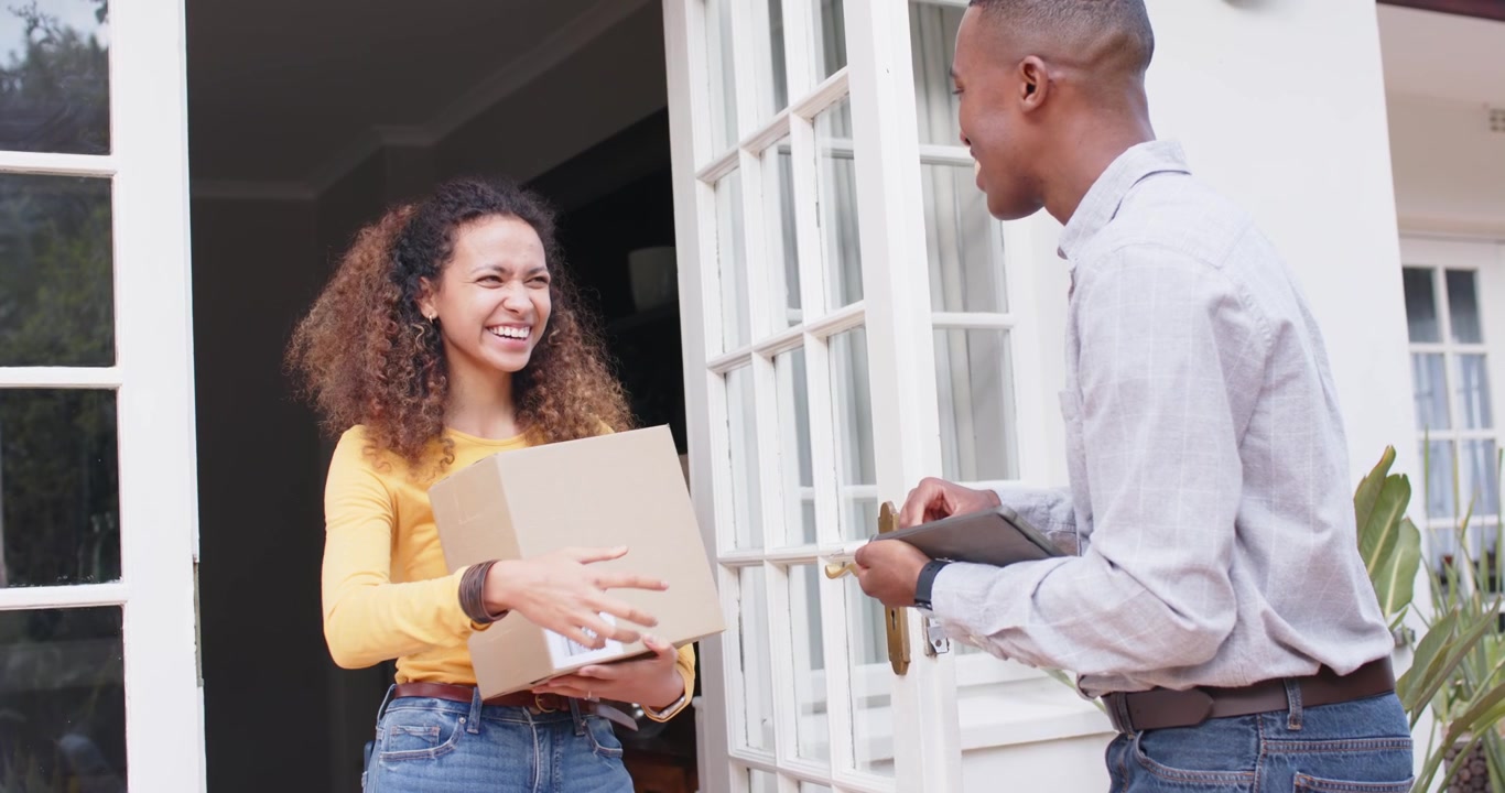 Courier offering tablet and pen, woman signing for delivery and bringing box inside at front door