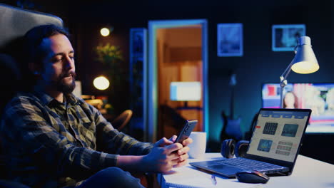 Man-takes-break-from-checking-financial-graphs-on-laptop,-playing-games-on-phone