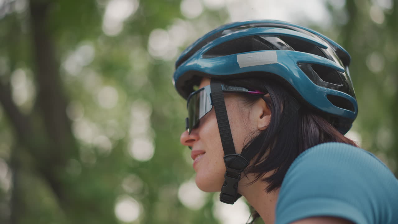 woman cyclist wearing blue helmet, smiling. leafy park background, reflective sunglasses, short hair, close profile portrait, gentle sunlight, relaxed pacing, training ride mood, optimistic