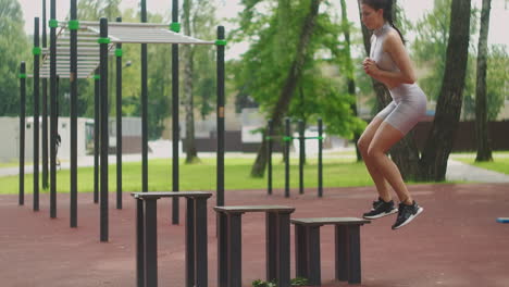 a young caucasian woman lifts her legs back while standing in a park on a sports field in the summer. a woman does sports in the summer alone in the park.