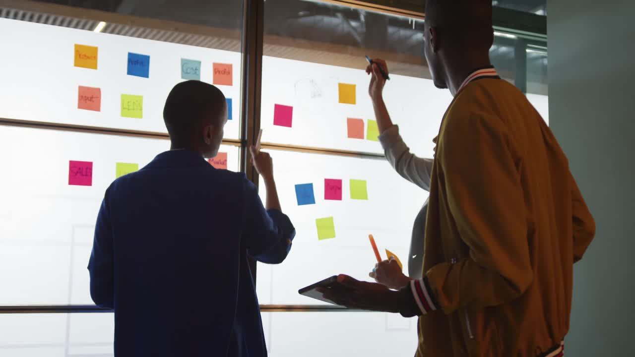 Diverse male and female creative colleagues brainstorming using tablet and writing on memo notes