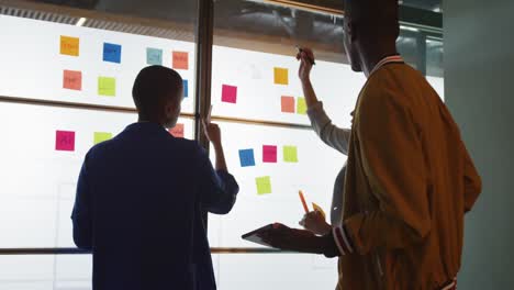 diverse male and female creative colleagues brainstorming using tablet and writing on memo notes