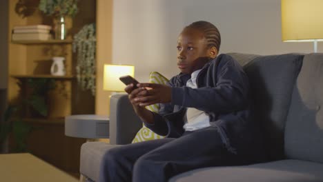 niño en casa sentado en el sofá por la noche viendo la televisión y mirando el teléfono móvil 1