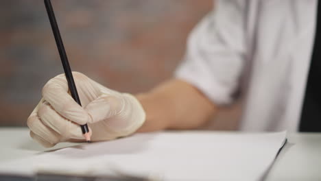 Doctor-in-gloves-writes-notes-listening-to-patient-in-clinic