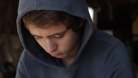 closeup of a sad, lonely and depressed teenage boy wearing a blue hoodie shirt with the hood up