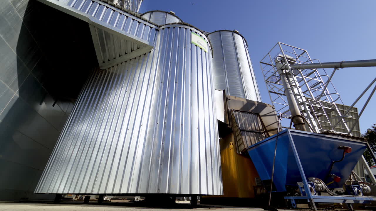 Metal granary at sunlight. Modern plant for processing agricultural harvest. Silver grain elevators in summer. Industrial complex for storing crop. Close-up.