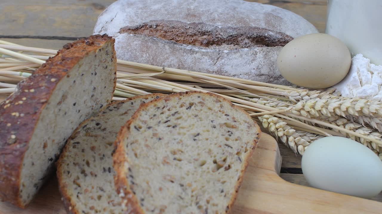 Loafs of bread, slices of bread, wheat flour, eggs and ears of grain on wood background. Rustic and rural concept. Close up. Flat lay
