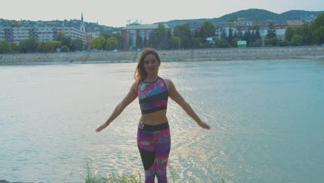 atractiva mujer atlética haciendo yoga en la naturaleza junto al río, haciendo pose de árbol con signo de namaste, cámara lenta