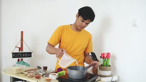 asian young man pouring water into saucepan on the stove in first process to making instant noodle at home