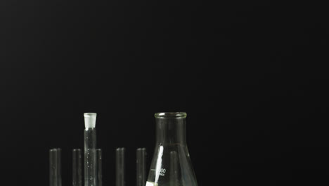 Coloured-liquids-in-flasks-with-test-tubes-in-stand-on-black-background-with-copy-space,-slow-motion