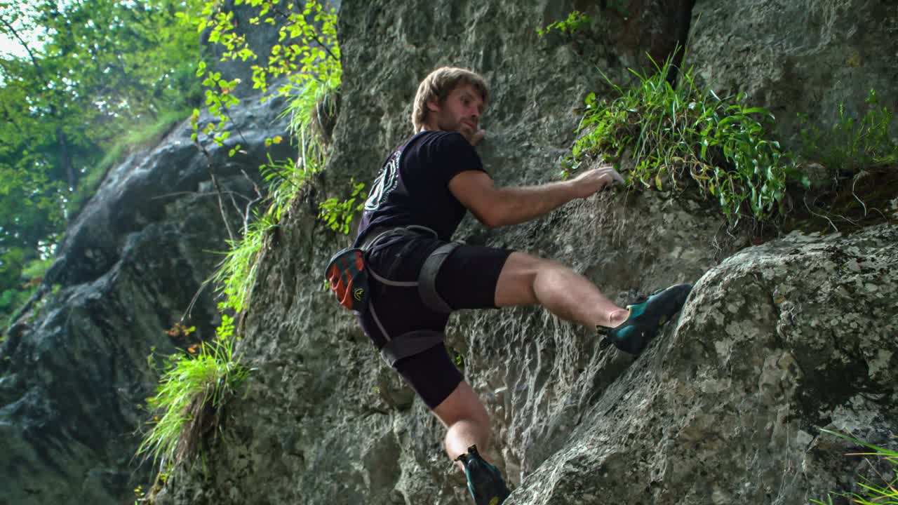 Young adventurous rock climber, climbing the steep rocks without any ropes. Concept of adventure and extreme sports. View from below