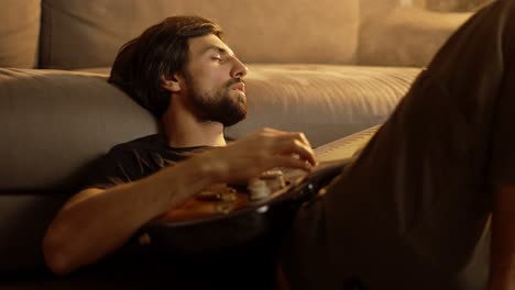 Man-playing-on-guitar-while-sitting-on-the-floor-in-smoked-room-with-closed-eyes