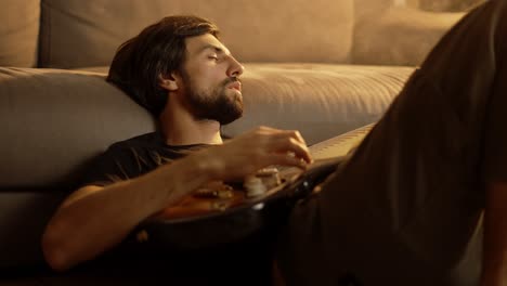 Hombre-Tocando-La-Guitarra-Sentado-En-El-Suelo-En-Una-Habitación-Ahumada-Con-Los-Ojos-Cerrados