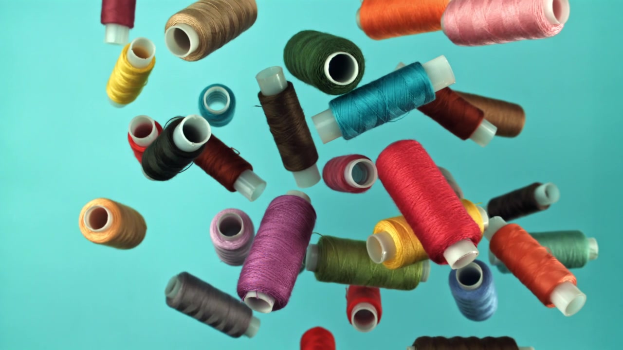 Colorful Spools of Thread Falling in Slow Motion on Blue Background