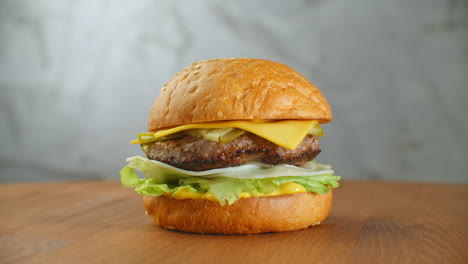 Great-Burger-with-beef-cutlet-tomatoes-mushrooms-and-cucumbers-with-melted-cheese-rotates-on-a-wooden-Board-on-light-background.