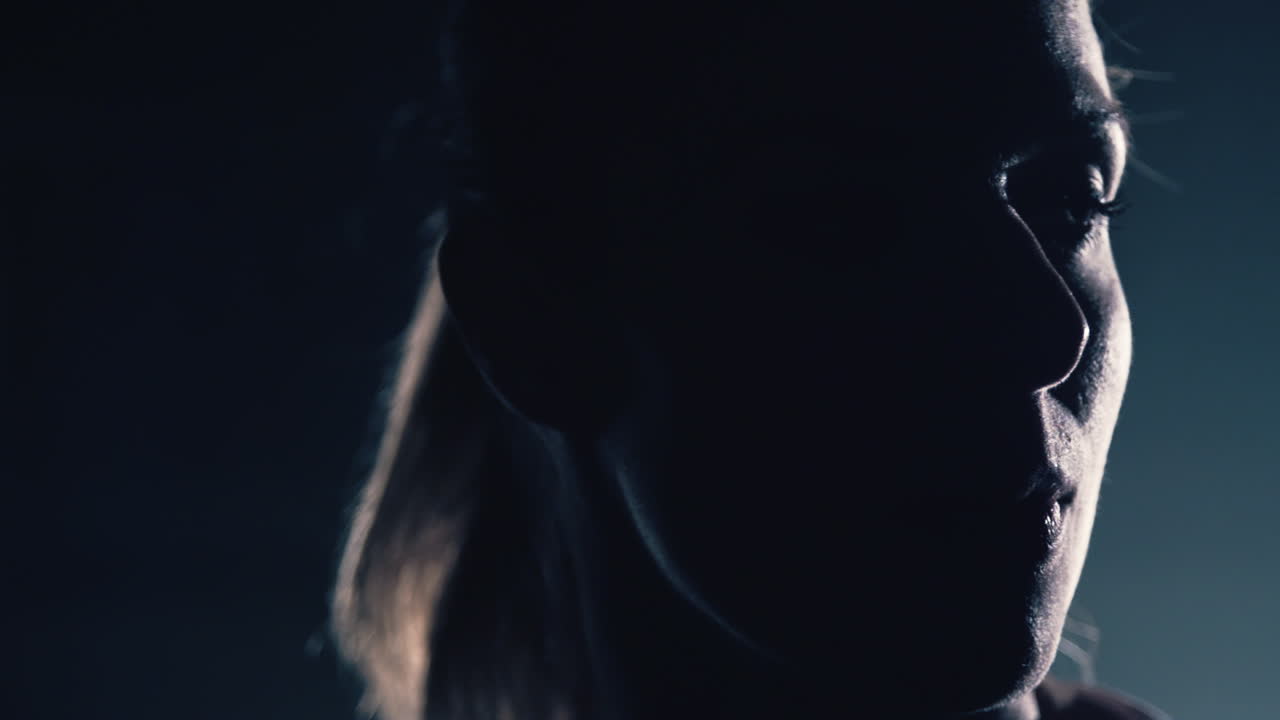 Swedish young woman turns around and faces the spotlight alone in the dark. Close up shot in slow motion.