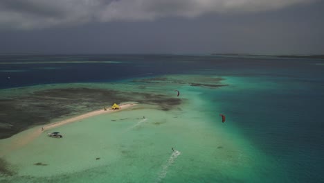 Kitesurfers-ride-waves-near-a-small-sandy-island-with-turquoise-waters-and-dark-clouds-above