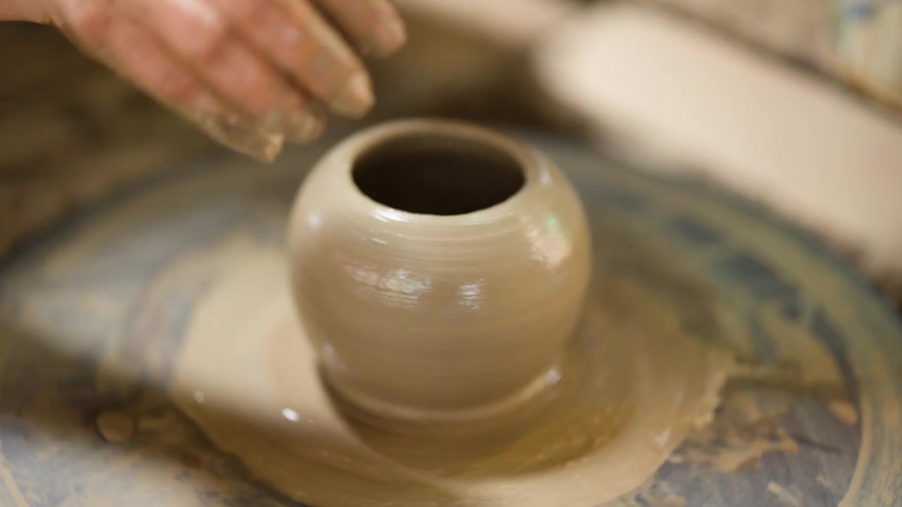 Close-up of potter's hands molding wet clay on a spinning wheel in Nonthaburi, Thailand.