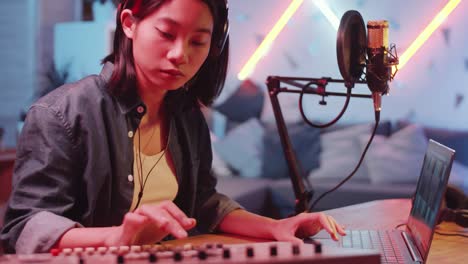 asian female musician using sound mixer and laptop in home recording studio