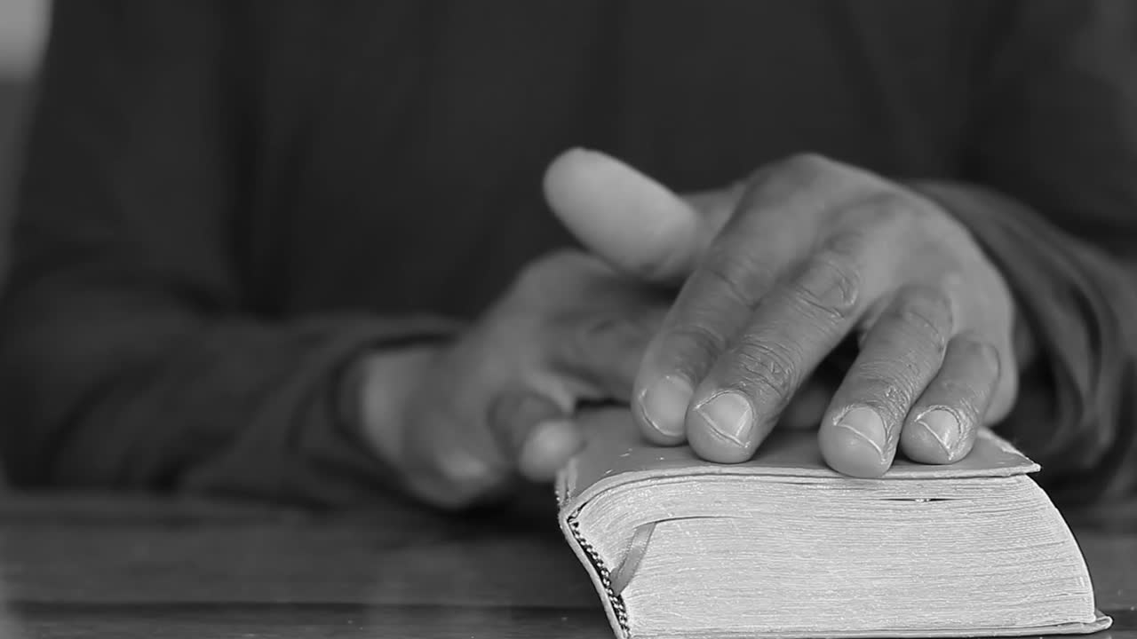Modlení se se sepjatýma rukama se svatou biblí na stole s lidmi. Stock videozáběr.