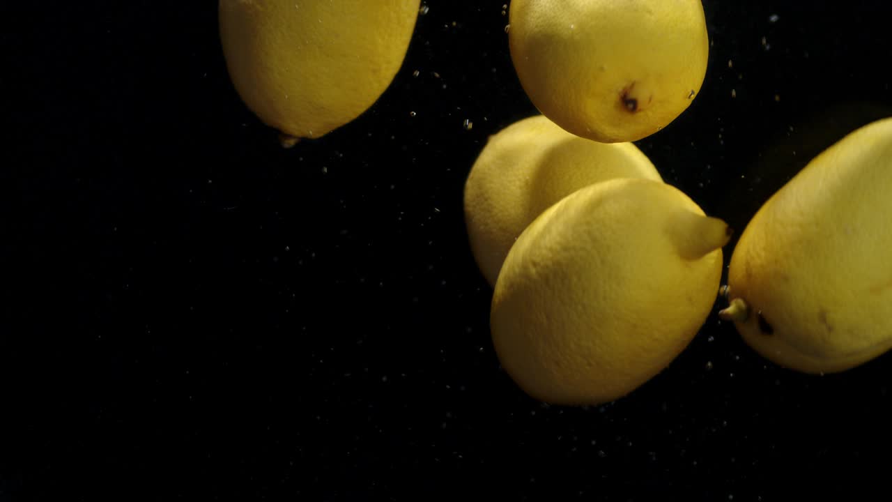 Whole fresh lemons are falling under water with air bubbles.