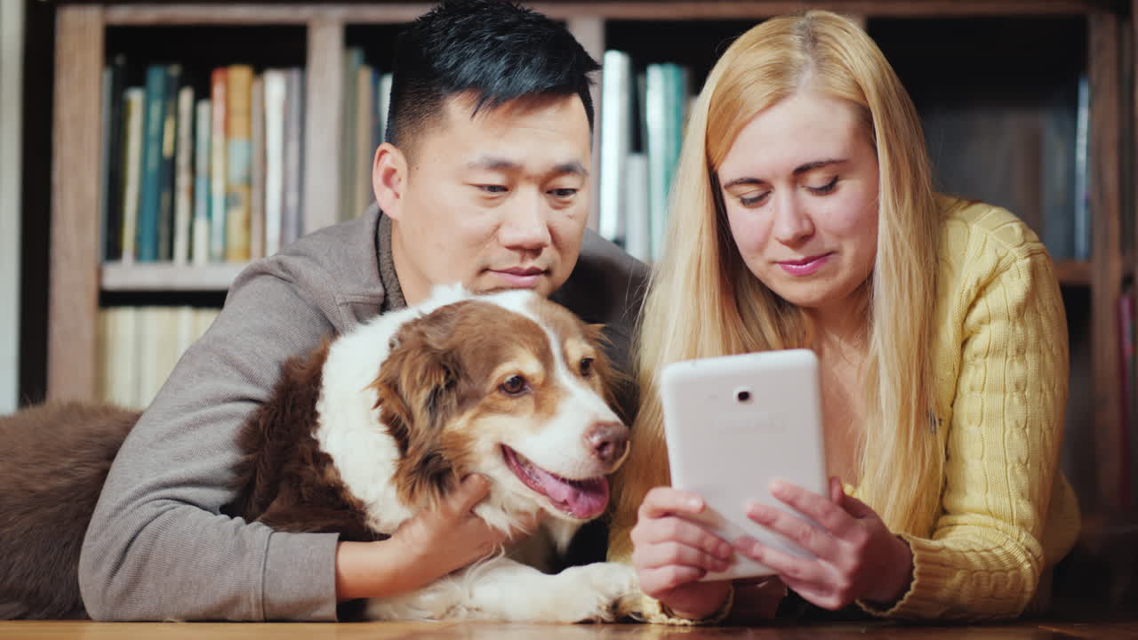 개를 사용하는 젊은 부부는 개와 함께 바닥에 누워 태블릿을 사용합니다