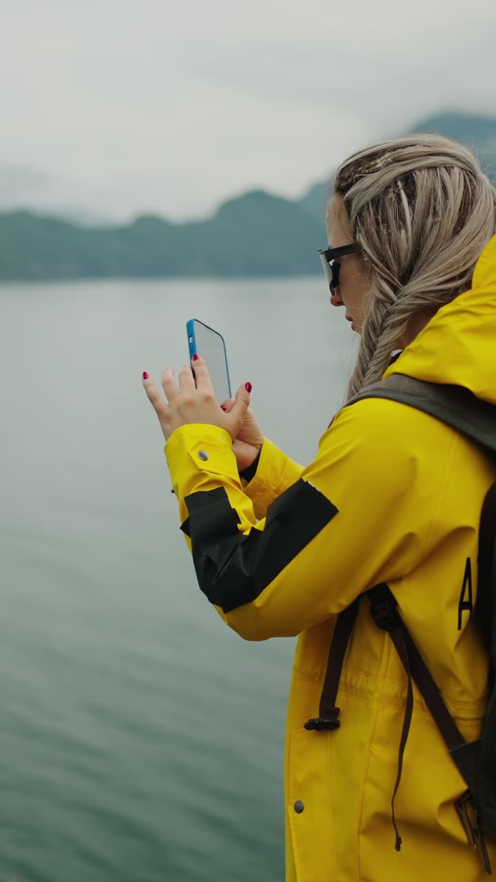 Woman in Yellow Raincoat Taking Photo with Smartphone by Lake