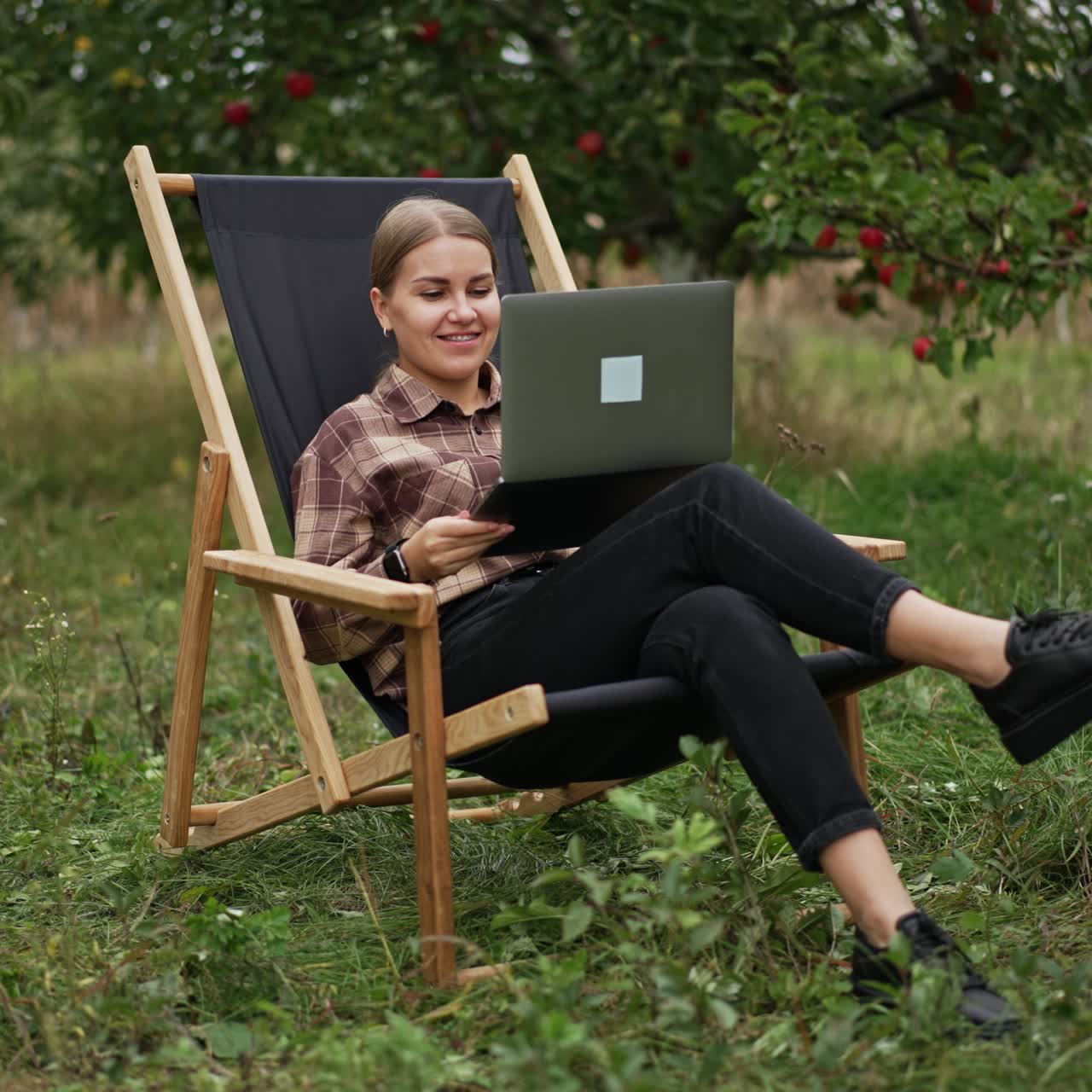 Lavorare online da remoto tramite internet. Giovane donna felice seduta in giardino che lavora al laptop, godendosi la natura e l'aria fresca. Concetto di lavoro freelance