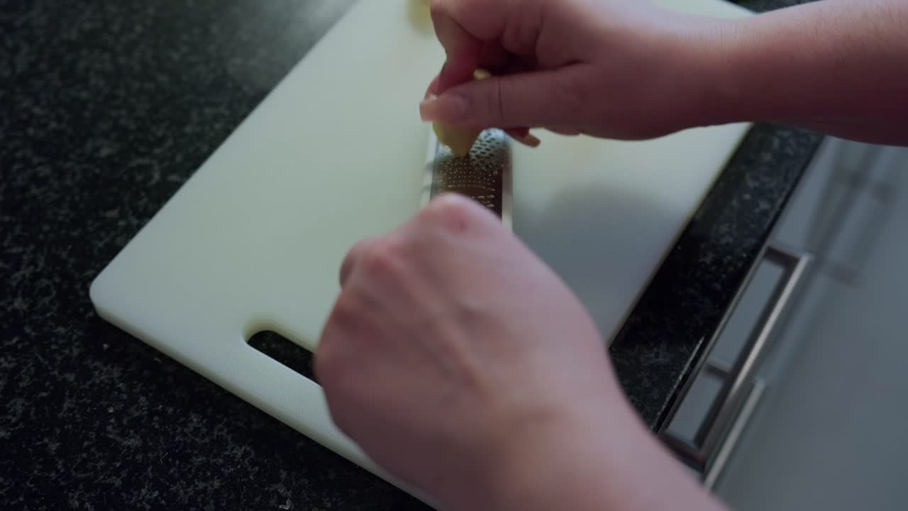 Woman's hands grating ginger on a white board, interior