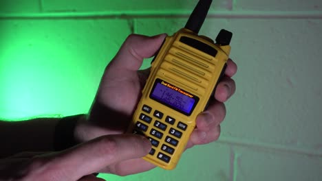 ingresando una frecuencia en una radio amateur de mano amarilla y luego transmitiendo y recibiendo contra un fondo verde