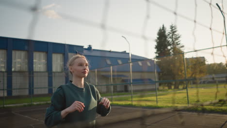 lady in green sweater playing volleyball outdoors, focused and ready to serve or pass, with building visible in background, captured in a vibrant setting with clear skies and sunlight