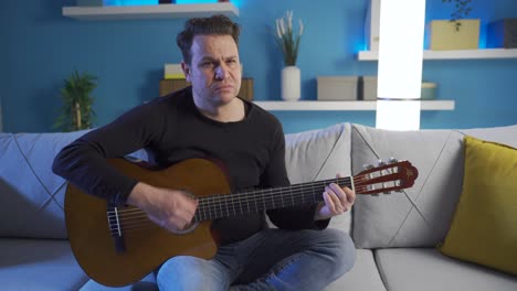 hombre frustrado sentado en el sofá tocando su guitarra triste y decepcionado.