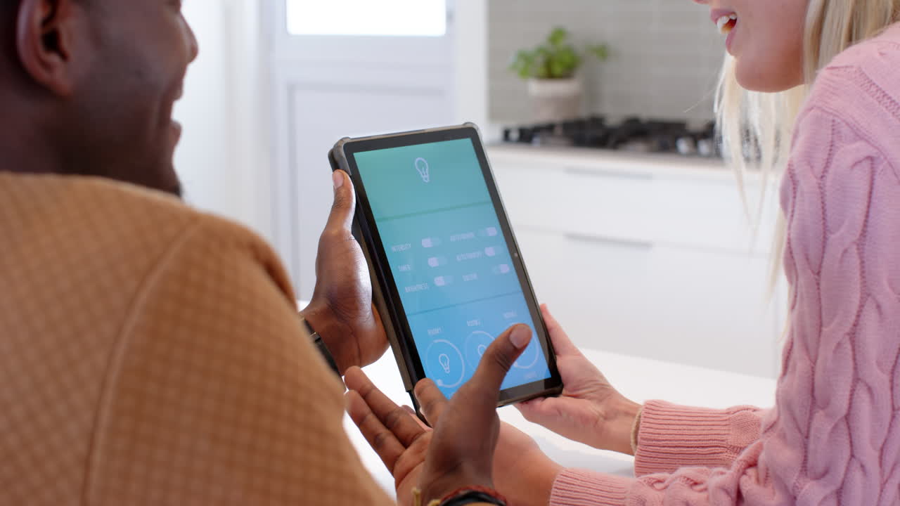 diverse couple using tablet to control smart home lighting in modern kitchen