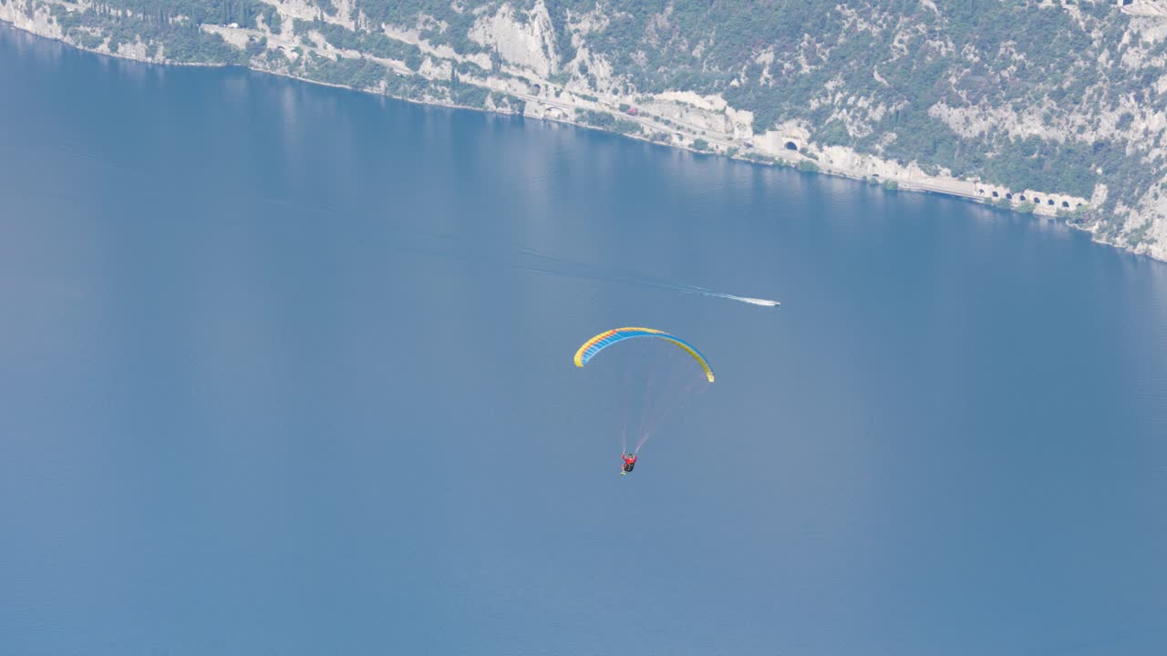 disparo de seguimiento de un hombre en parapente sobre el lago azul de garda en un día soleado de verano, italia
