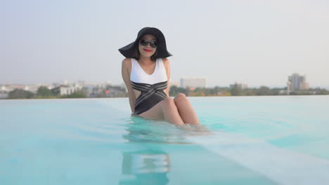 Asian-model-woman-sitting-at-the-edge-of-the-infinity-pool,-Front-view