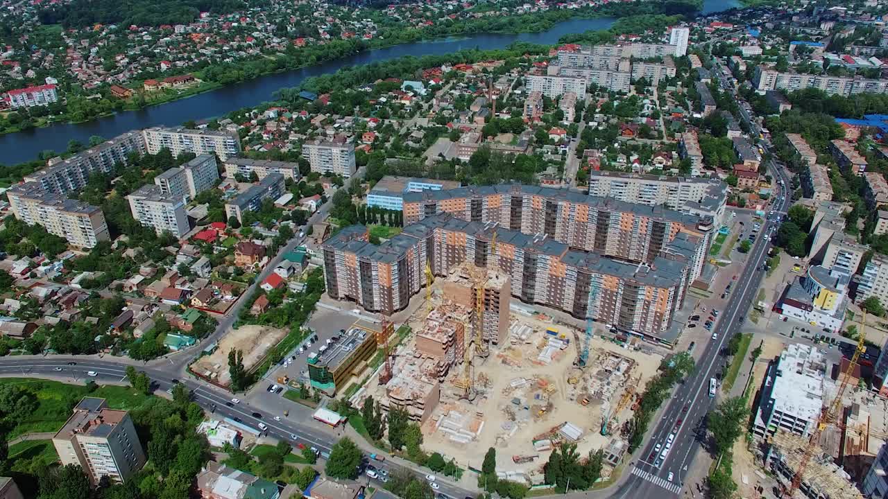 Construction site of a modern district in the city. Urban background with beautiful high-rise buildings, green trees and a blue river. Aerial view.