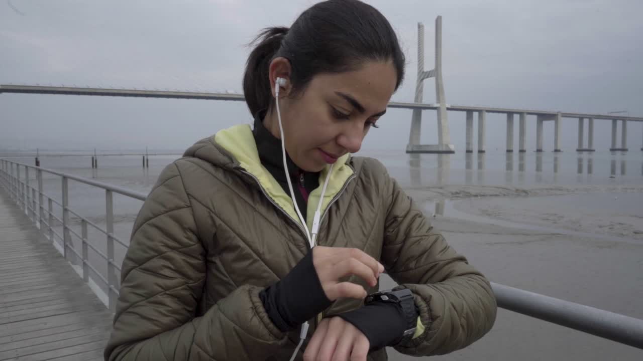 Giovane ragazza sportiva sorridente che imposta l'orologio sportivo al mare.