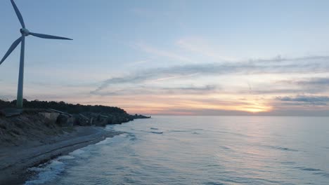 aerial establishing view of abandoned seaside fortification buildings at karosta northern forts on the beach of baltic sea in liepaja, sunset, golden hour, wind turbine, wide drone shot moving forward