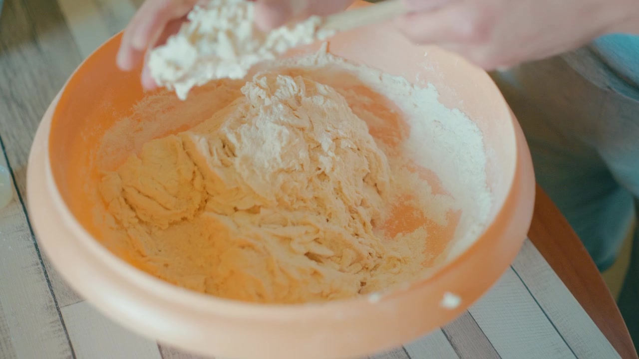 Close up shot of teenage hands kneading fresh sticky dough inside an orange bowl. Traditional bread making process, working with texture, culinary skills, cozy home kitchen lifestyle, 4k.