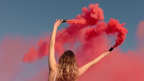 woman waving pink smoke bomb on beach at sunrise slow motion