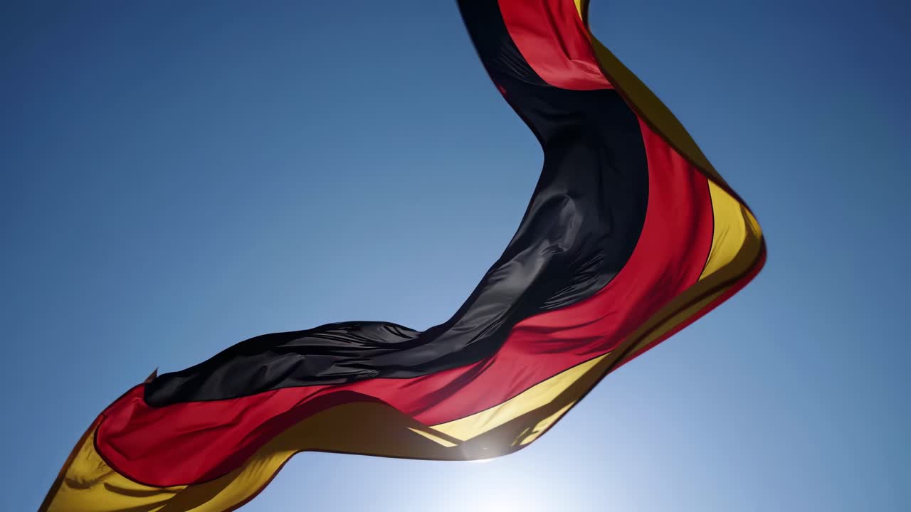 Low-angle shot of a German flag waving against a clear blue sky, capturing a dynamic and patriotic